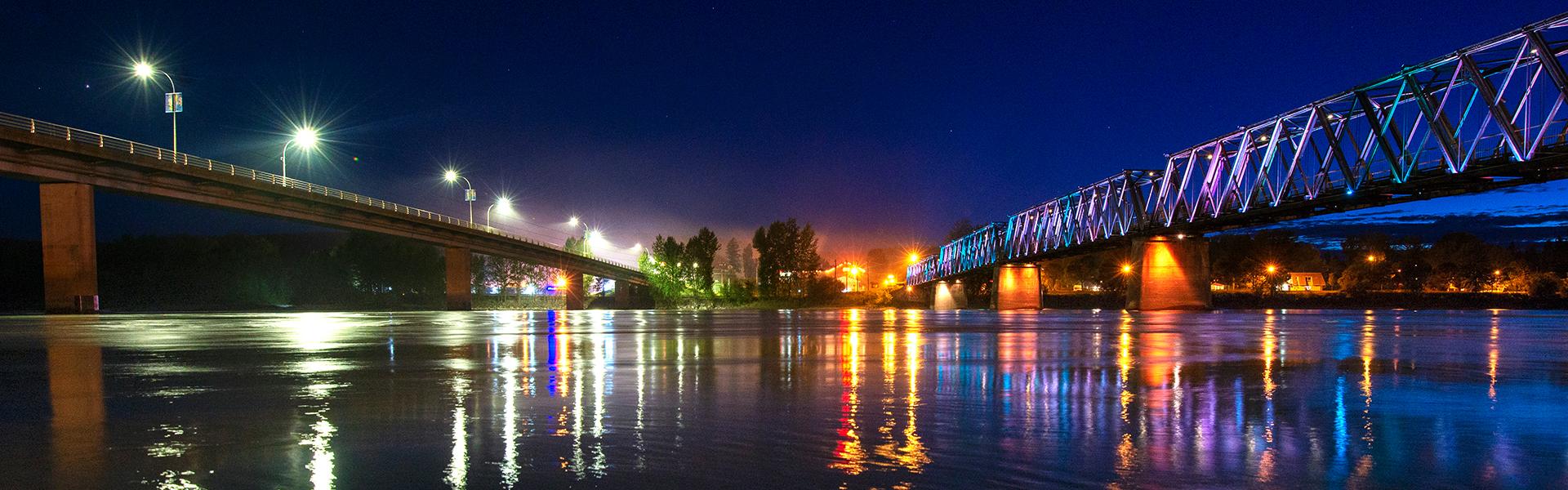Nigh view of two bridges lit up over the Fraser River
