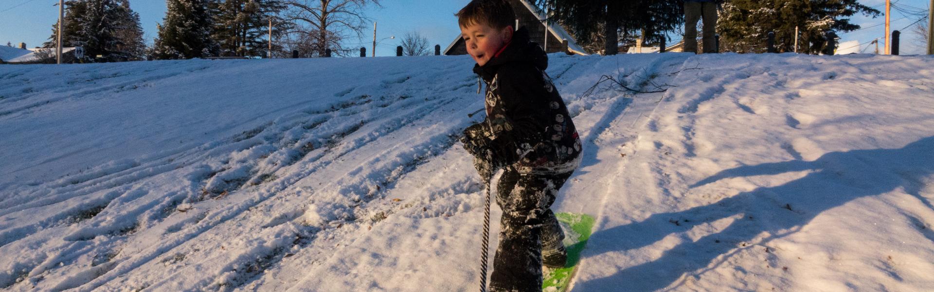 Young boy snowboarding down the hill at LeBourdais Park