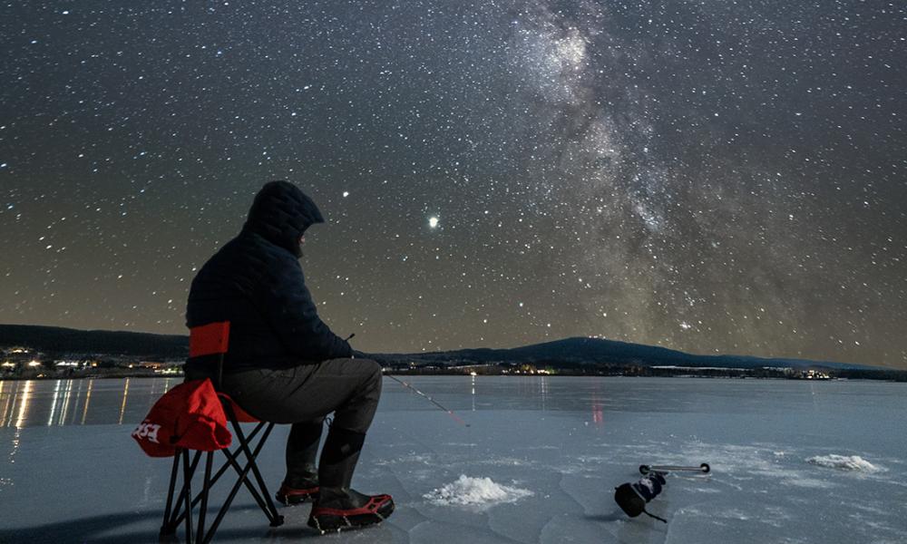 Person ice-fishing under the stars on the Dragon Lake