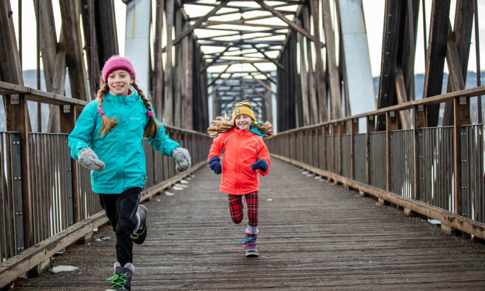 Two young girls dressed for winter running on the Fraser River Footbridge 