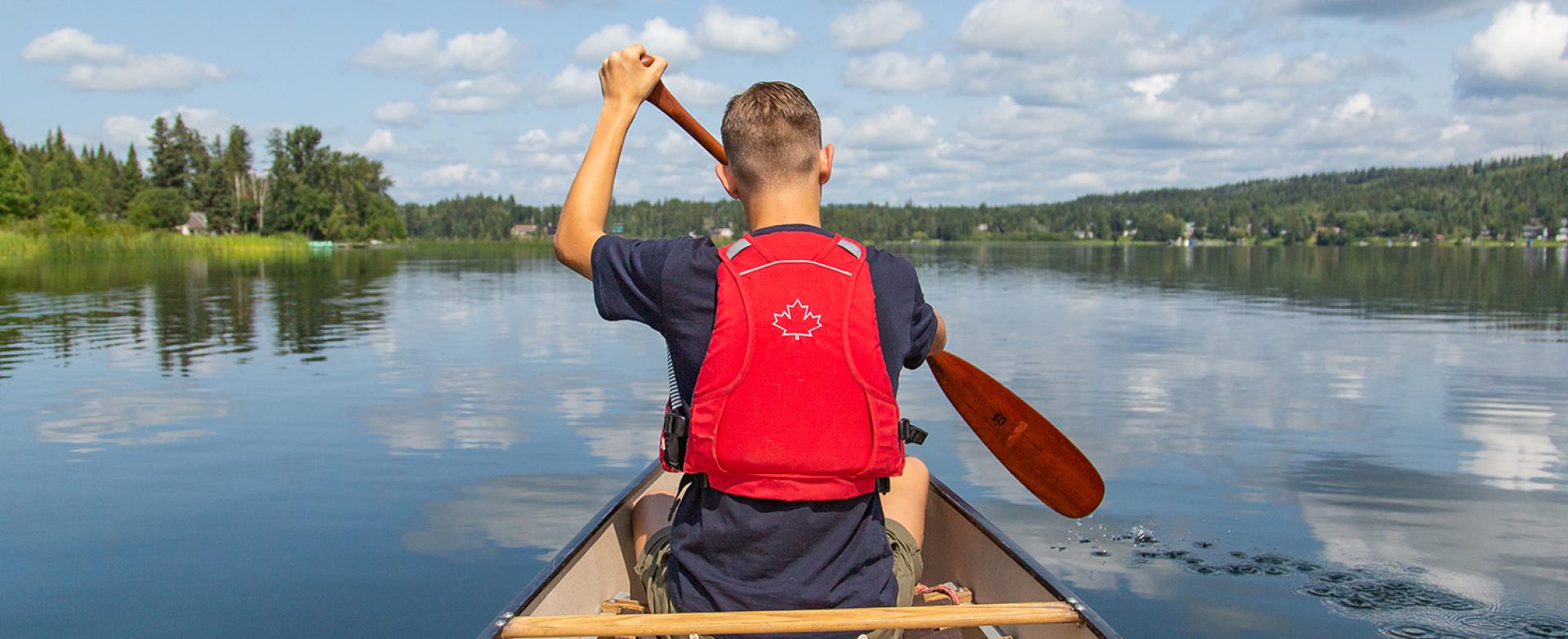 Man wearing a red life jacket canoeing on calm lake water