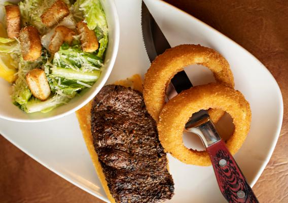 A plate a full rack of baby back ribs glazed in bourbon BBQ sauce served with onion rings & bowl of caesar salad 